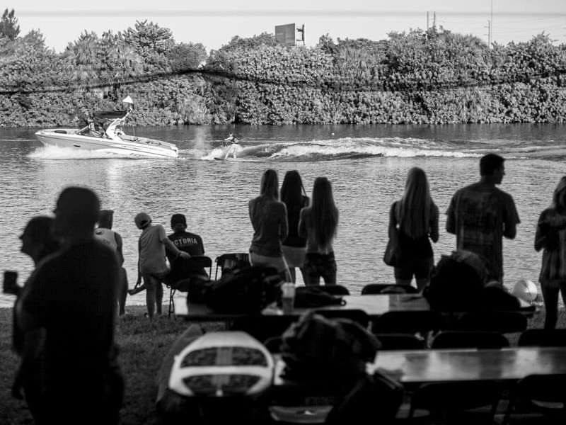 A black and white photo of surfers watching a boat in the water.