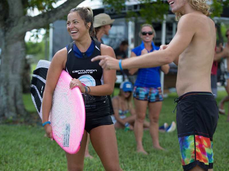 A group of surfers standing in a grassy area with surfboards.