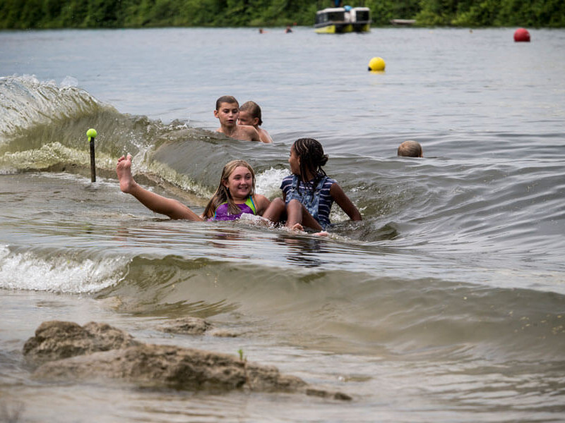 A group of kids participating in a wake surfing contest and impressing their fans with their skills on the surfboard.