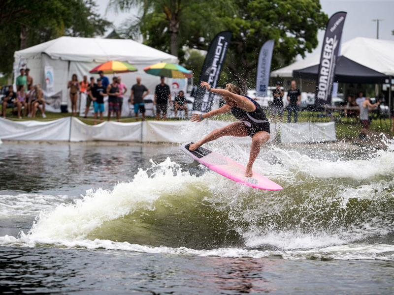 A woman is Wake surfing on a pink surfboard in the water.