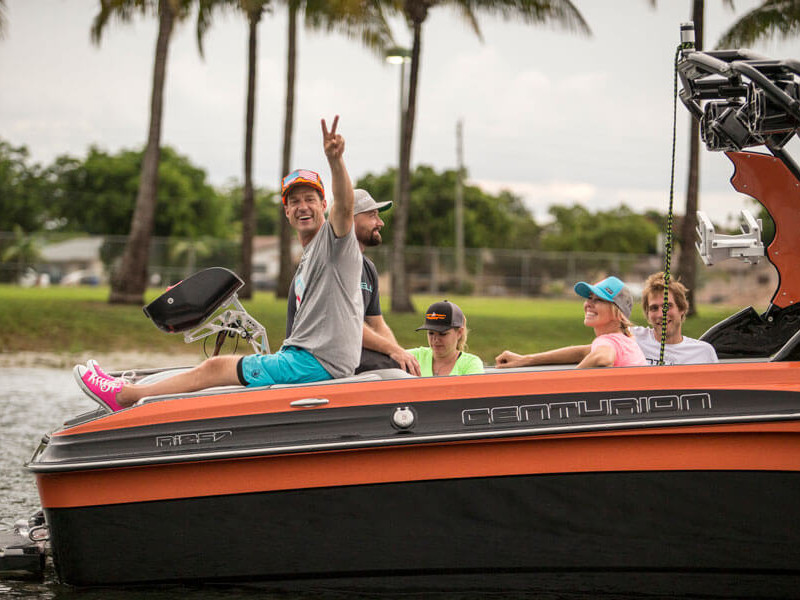A contest of wake surfing competition on a boat, with the participants enthusiastically waving to the camera.