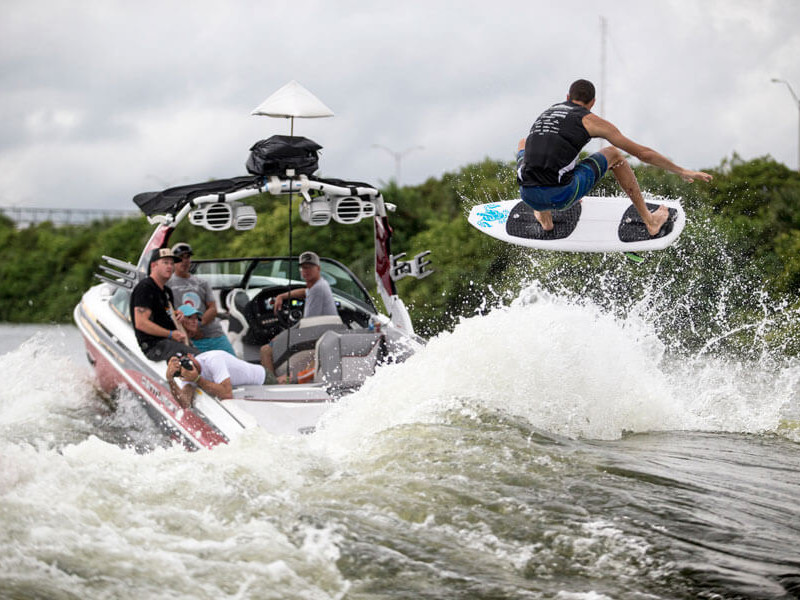 Competitors performing wake surfing to the amazement of fans on a boat.