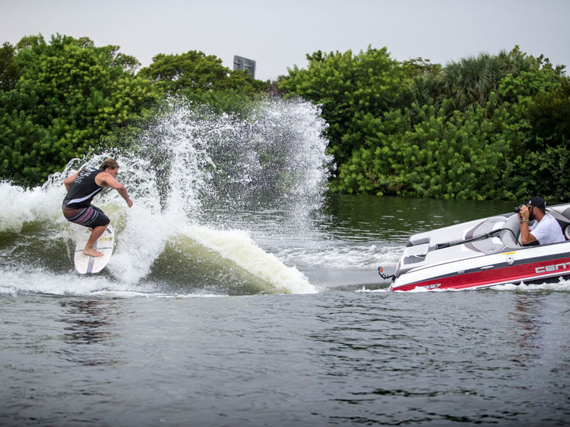 A man is competition in wake surfing, maneuvering on a surfboard with the support of fans.