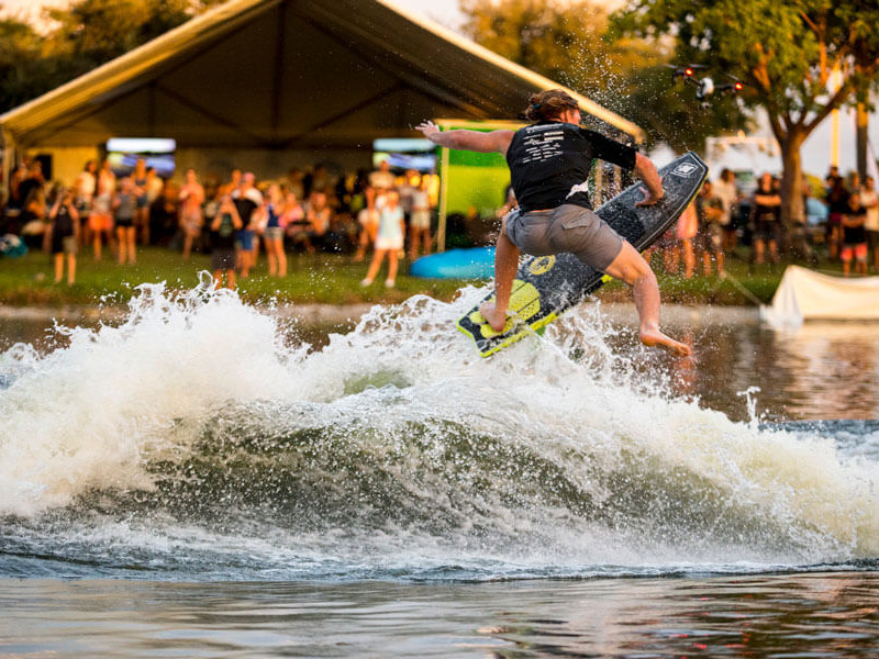 A man is competing in a wake surfing contest, riding a wave on a surfboard.