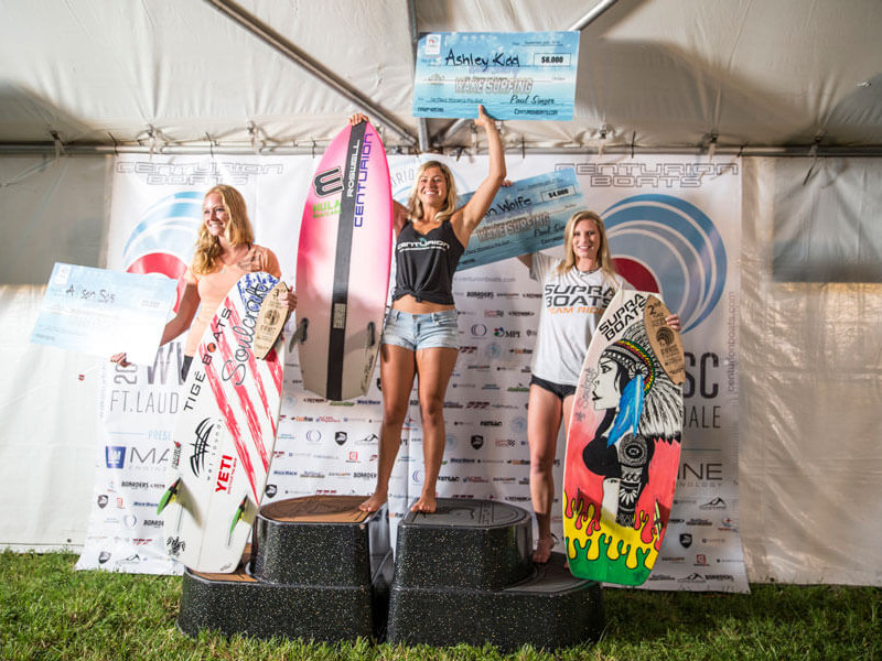 Three surfers standing on top of a tent with their surfboards.