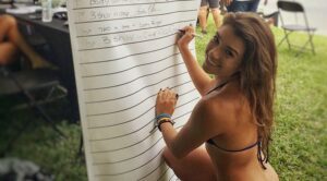 A woman writing on a white board while wearing a bikini, captivating surfers and fans.