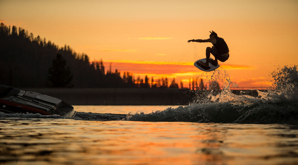 A wakeboarder, along with fellow surfers, jumps off a boat at sunset during an exhilarating competition.