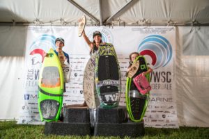 Three competitors standing on top of a podium with surfboards, participating in a wake surfing competition.