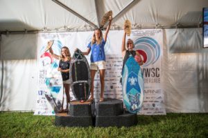 Three competitors standing on top of a podium with surfboards.
