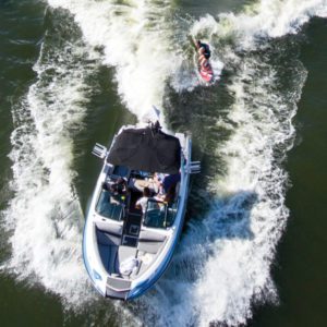 Wake surfing is a thrilling water sport that combines elements of surfing and boating. In this captivating aerial view, a skilled surfer is seen gracefully riding a surfboard behind a boat, with