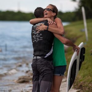 Two surfers hugging in front of a body of water after a wake surfing competition.