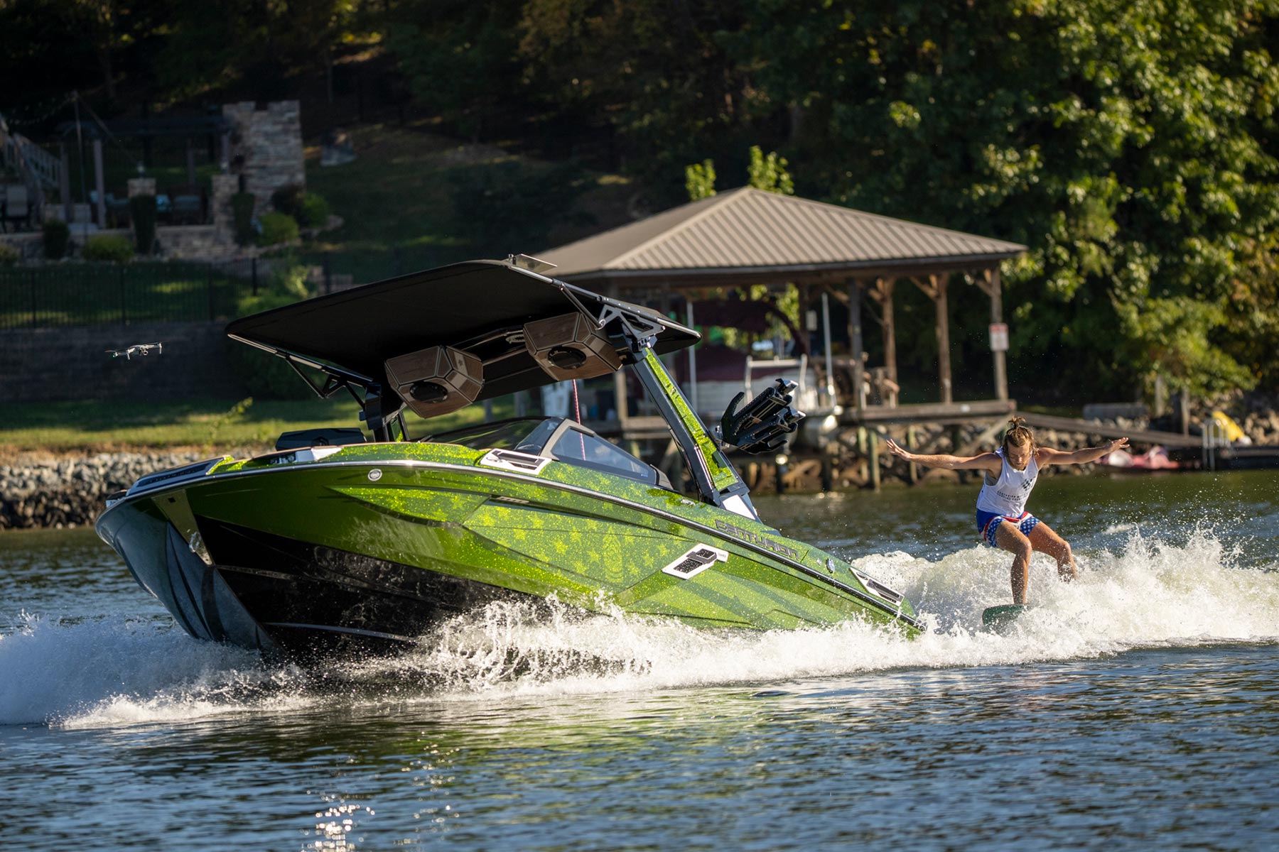 A woman is wake surfing on a green boat.