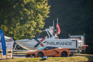 An orange corvette parked next to a boat used for wake surfing.