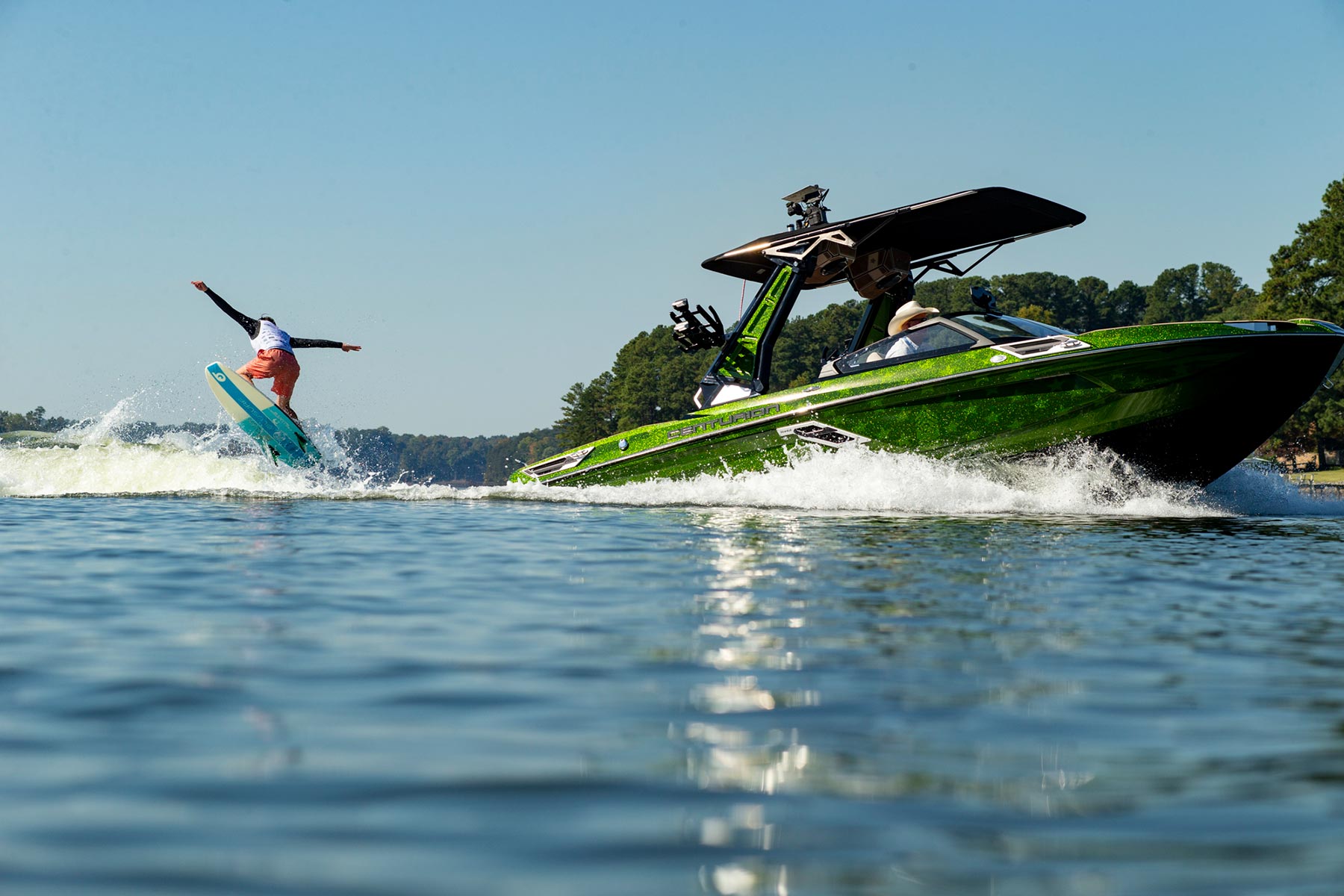 A competitor is riding a wakeboard on a green boat in an intense contest.