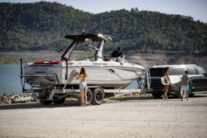 A group of wake surfing enthusiasts standing next to a boat on a trailer.