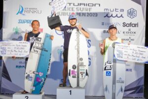 Three competitors standing on top of a podium with their surfboards, showcasing their wake surfing skills.