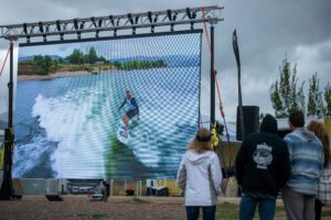 A large screen displaying a surfboarder riding a massive wave during an exhilarating wake surfing contest, captivating fans.