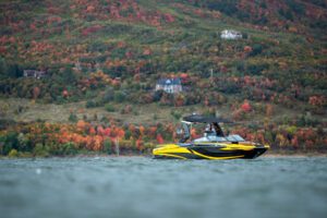 A yellow and black jet ski on a lake in the fall, with wake surfers riding the waves.