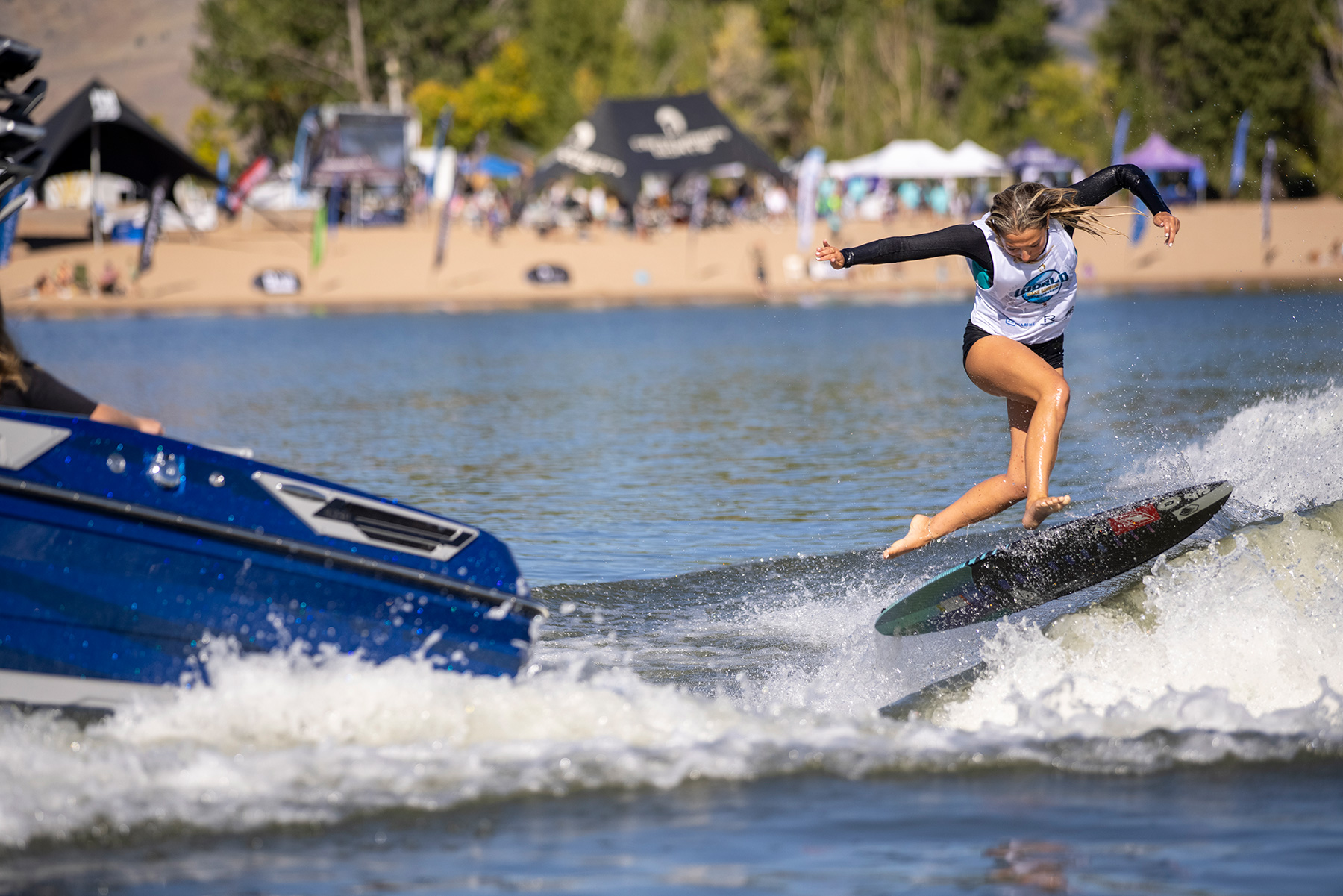 A woman is riding a surfboard on a lake, competing against other surfers.