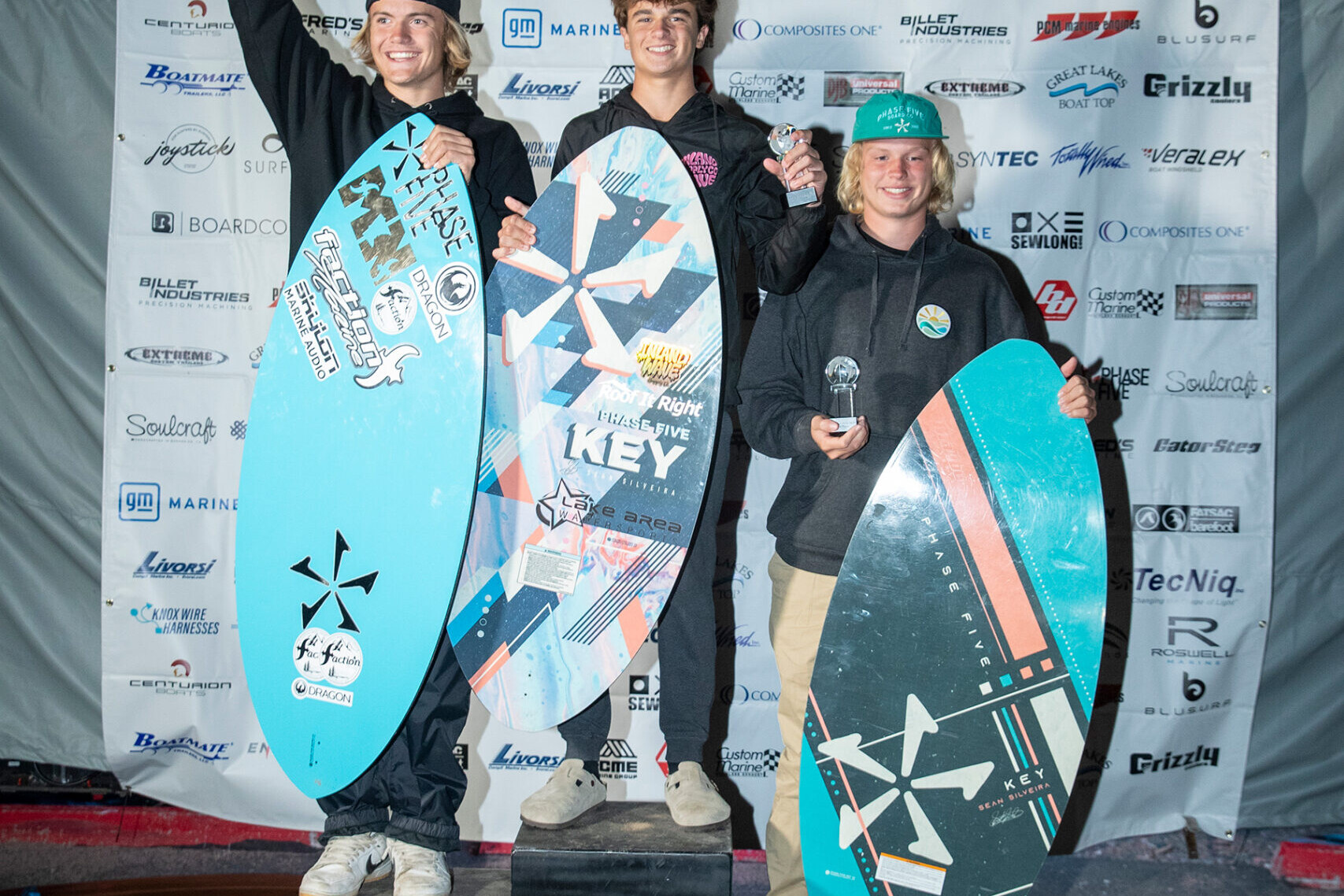 Three surfers competing on a podium in wake surfing.