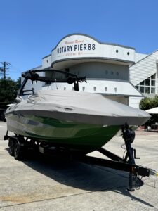 A green and white boat covered with a protective tarp is parked on a trailer in front of a building labeled "Rotary Pier 88," reminiscent of the sleek designs often seen at the Japan Open.