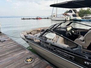 A black Centurion Wake Surf boat docked at a wooden pier with a calm lake and several other boats in the background, the serene scene reminiscent of peaceful mornings at LIB Resort.