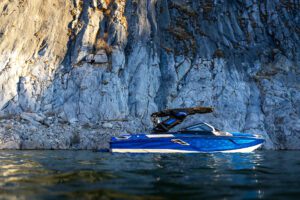 The Centurion Ri Seris, a blue boat, floats on water near a tall, rocky cliff under natural light.