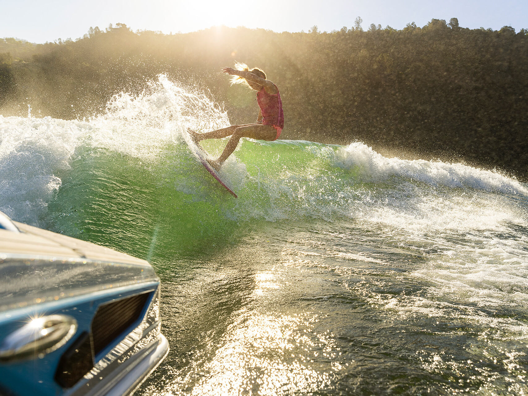 Surfer riding a wave with a bright sun in the background, carving through the water near The Centurion Ri Seris boat.