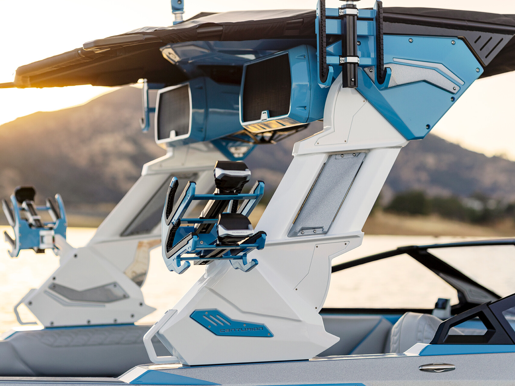 Close-up of a modern boat's wakeboard tower on The Centurion Ri Series, showcasing speakers and board racks against a stunning sunset view over the water.