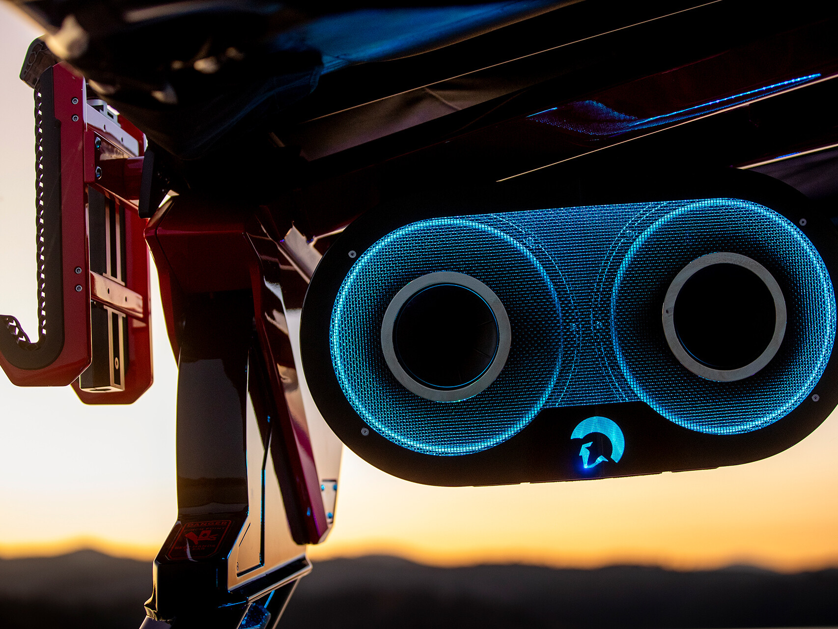 Close-up of The Centurion Ri Series speaker system, bathed in blue light on a vehicle at sunset, with a mountainous landscape in the distance.