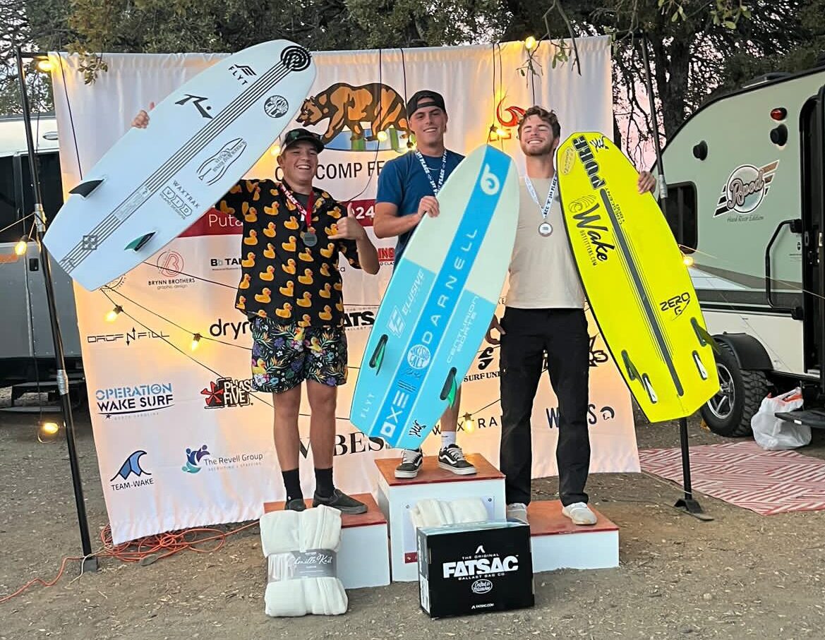 Three people stand on a podium holding large wakeboards, celebrating their victory at the WSWS Festival Finals. Behind them, a branded Centurion backdrop adds to the triumphant atmosphere.