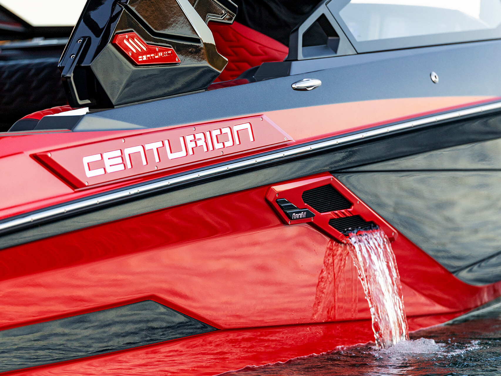 Close-up of a red Centurion boat from the Centurion Ri Series on the water, with water flowing out from a rectangular outlet on the side of the hull.