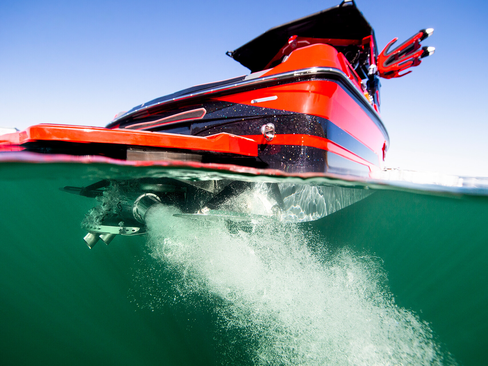 A red and black Centurion Ri Series motorboat is seen from a split underwater and above-water angle, showing its stern, propeller, and bubbles in greenish water.