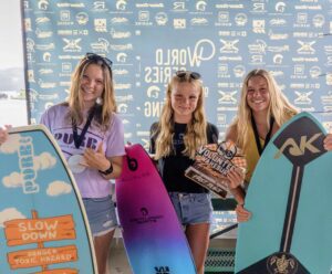 Three young women holding skimboards and a youth skimboarding award, standing in front of a Centurion WSWS Wake Surf Classic 2025 Finals event backdrop.