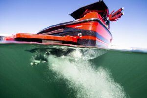 A partially submerged view of a red Centurion Ri Series motorboat releasing bubbles into green water, with a clear sky visible above the surface.