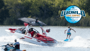 A wake surfer rides behind a Centurion boat on a lake, with spectators nearby. The image includes a logo for the 2025 Centurion World Wake Surfing Championship in Fort Lauderdale, Florida.