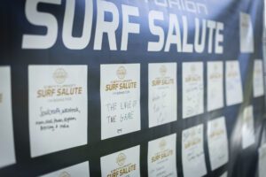 Close-up of a display board with cards titled "Centurion Surf Salute," featuring handwritten reasons for participating, like "The love of the game," at the Wake Surfing Championship hosted by Centurion World and GM Marine.