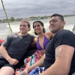 Three people sit together on a Centurion Boat, smiling at the camera; water and houses on Lake Conroe are visible in the background under a cloudy sky.