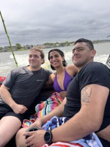 Three people sit together on a Centurion Boat, smiling at the camera; water and houses on Lake Conroe are visible in the background under a cloudy sky.