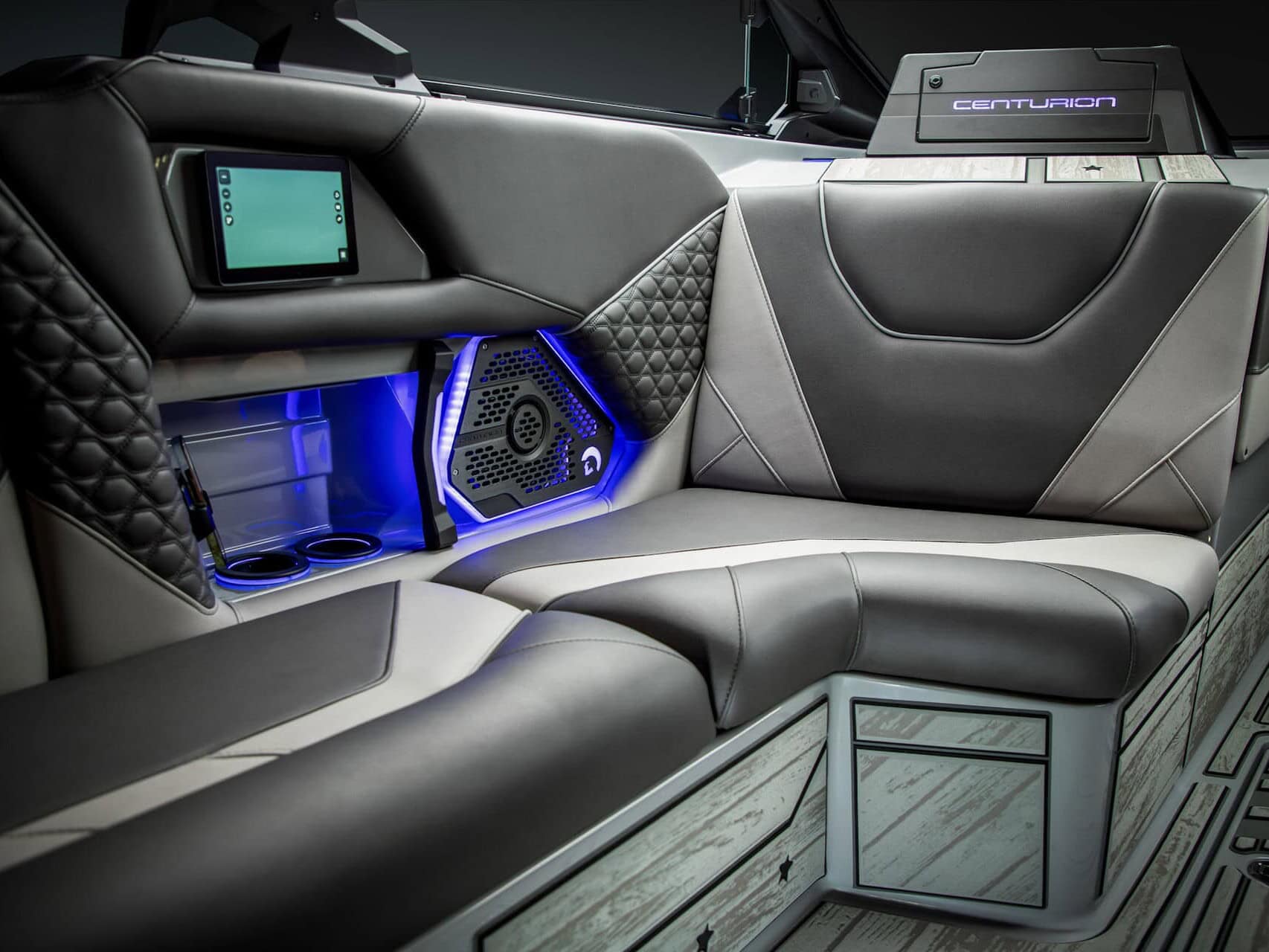 Modern boat interior with black and gray cushioned seating, blue LED accent lighting, cup holders, speaker, and a small screen, with