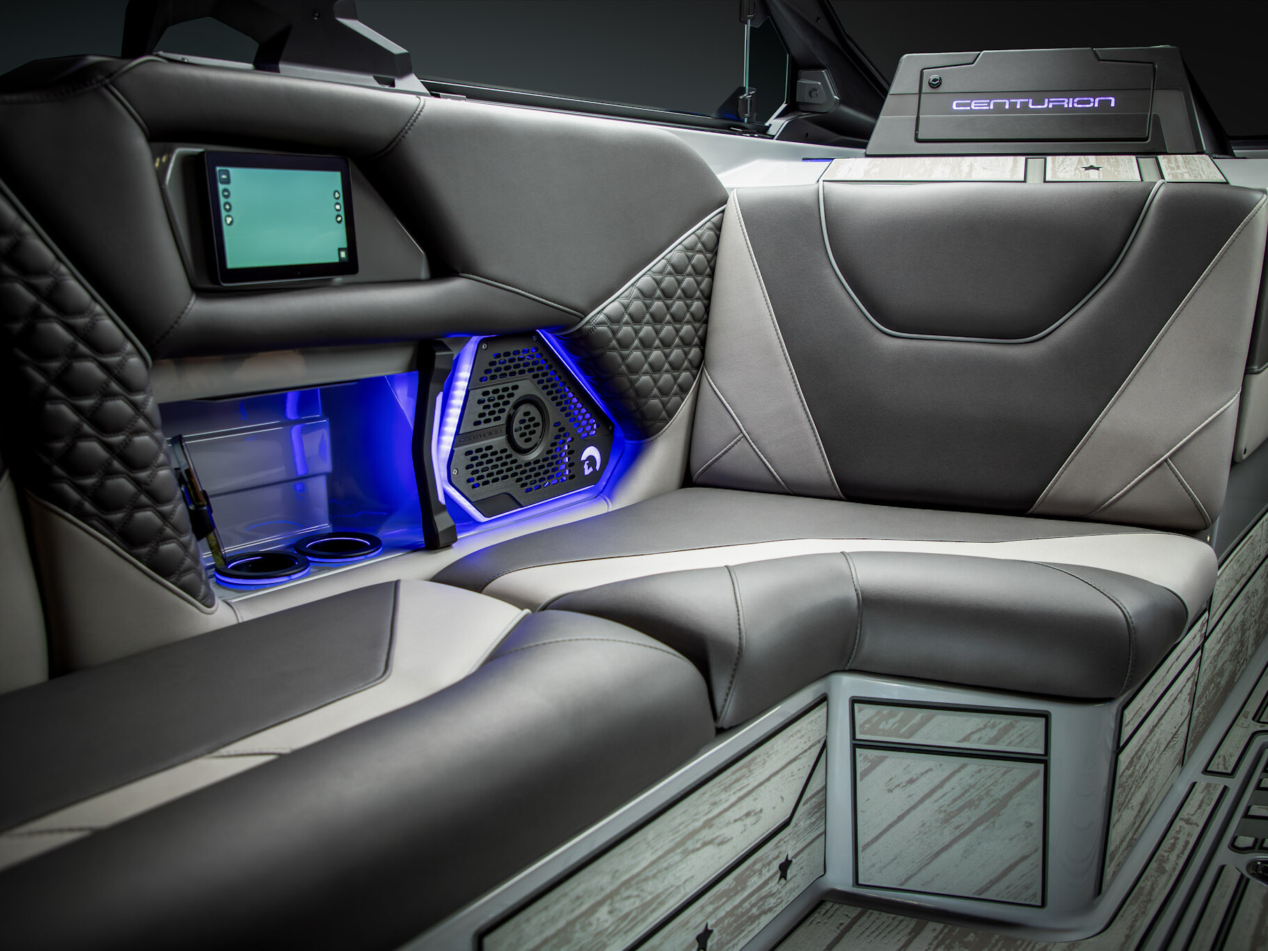 Modern boat interior with black and gray cushioned seating, blue LED accent lighting, cup holders, speaker, and a small screen, with