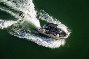 A person wakeboards behind a motorboat, possibly from The Centurion Ri Series, on green water, leaving curved white waves in their wake.